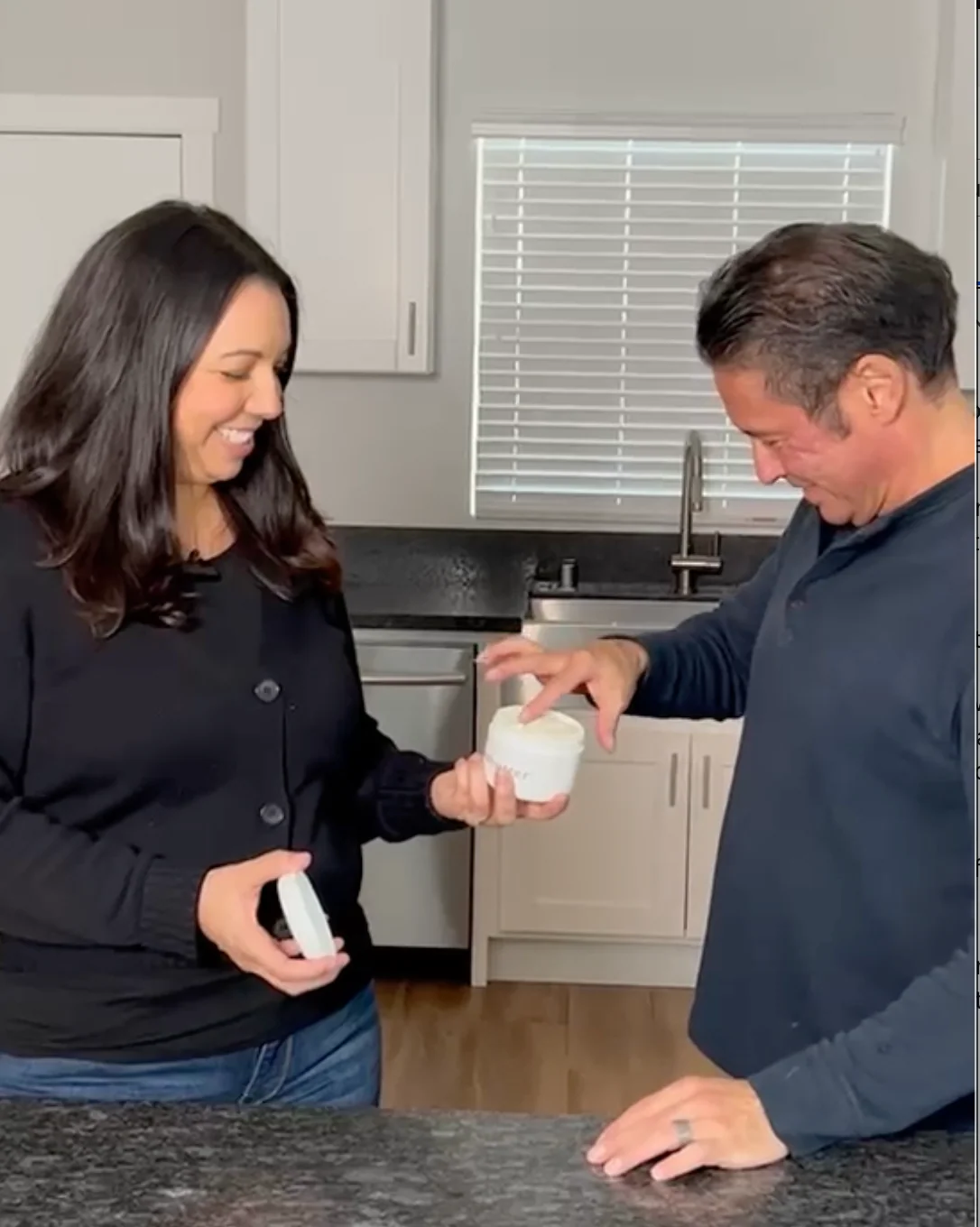 Our founder holds an open jar of beabutter while Ric dips his fingers into the cream in their kitchen